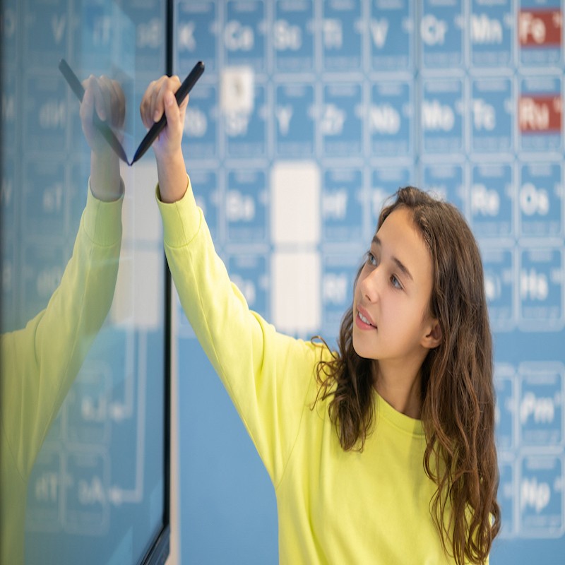 Smart school. Long-haired smiling girl standing drawing with marker on blackboard in classroom during lesson